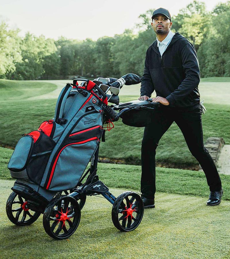 BagBoy Quad Pro Golf Push Cart in Navy/Red - male golfer pushing cart with golf bag & clubs on the fairway