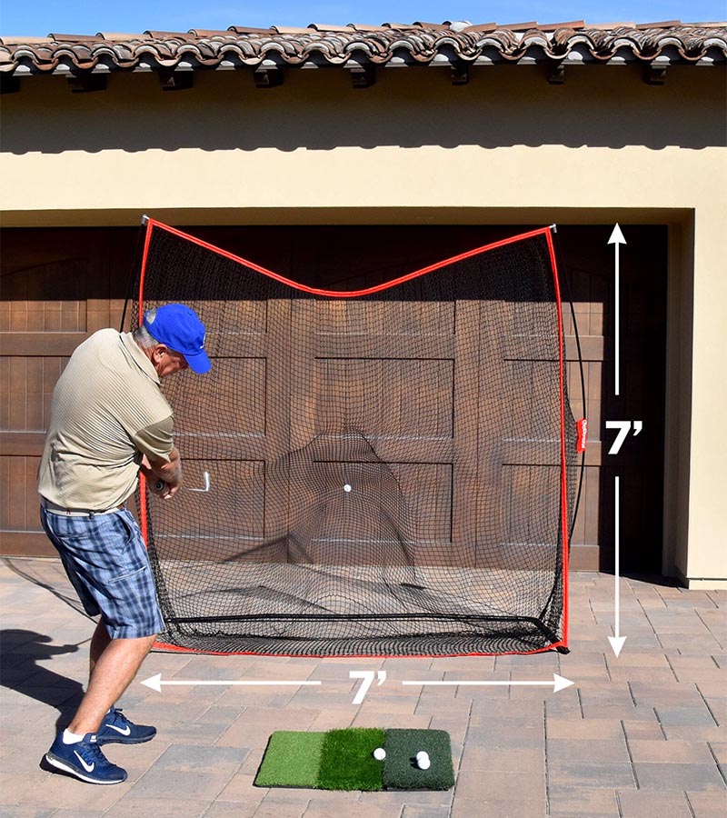 GoSports Golf Practice Hitting Net 7 Ft X 7 Ft - Golfer practicing in driveway with wood garage door behind the net with 7'x7'dimensions shown with white arrows