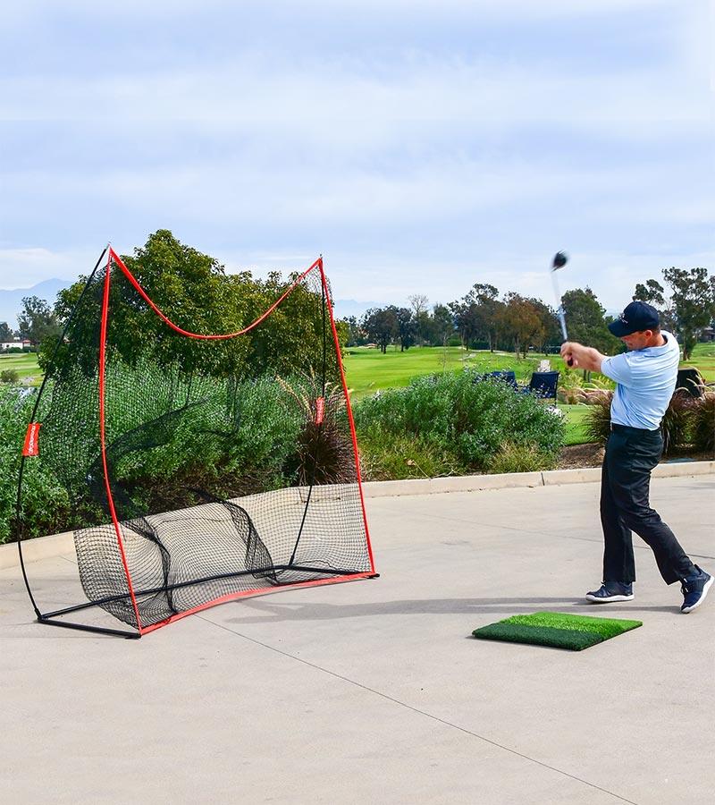 GoSports Golf Practice Hitting Net 7 Ft X 7 Ft - Golfer practicing outside. Golf course in the background.