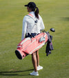 Sunday Golf Ryder Full Size Stand Golf Bag in Coral – female golfer carrying the bag on a course