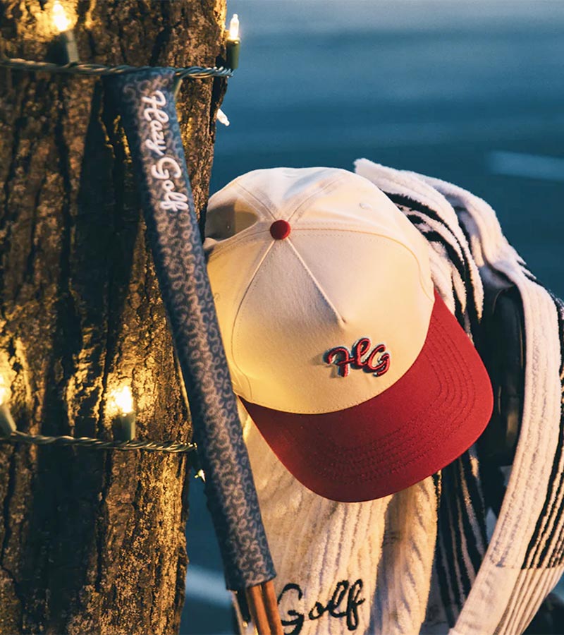 Hazy Golf HG 2 Tone Cardinal and Bone Snapback - front/top view with Cardinal red visor placed on the top of a cart with a Hazy Alignment stick cover in the foreground