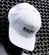 Hazy Golf: Hazy X Tremont Dune Hat  in white front view with logo across the front crown in black. Hat attached to metal geometric fencing
