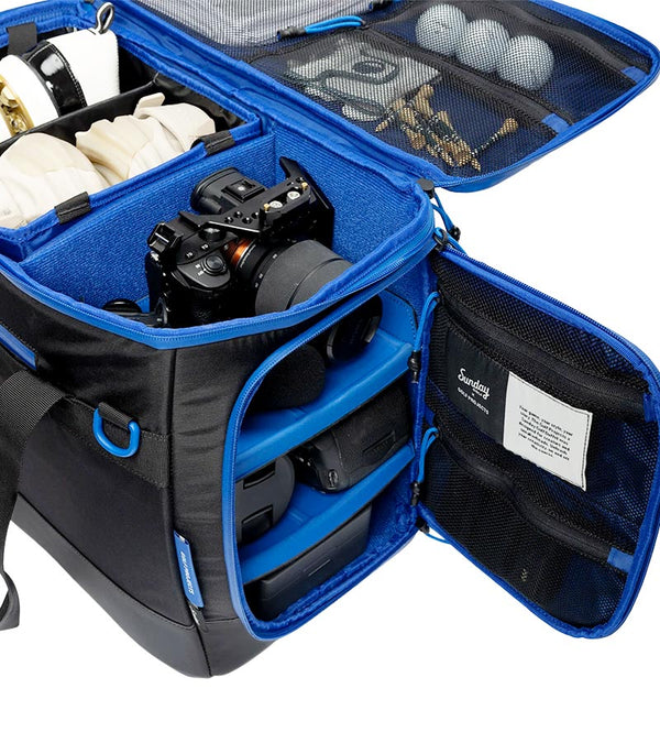 Sunday Golf Creator Duffle Bag in Black with blue accent details shows open  compartments  and pockets for camera  and camera equipment, golf balls, and other items 
