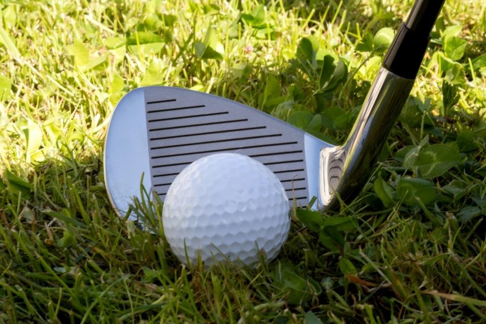 golf iron behind ball in grass