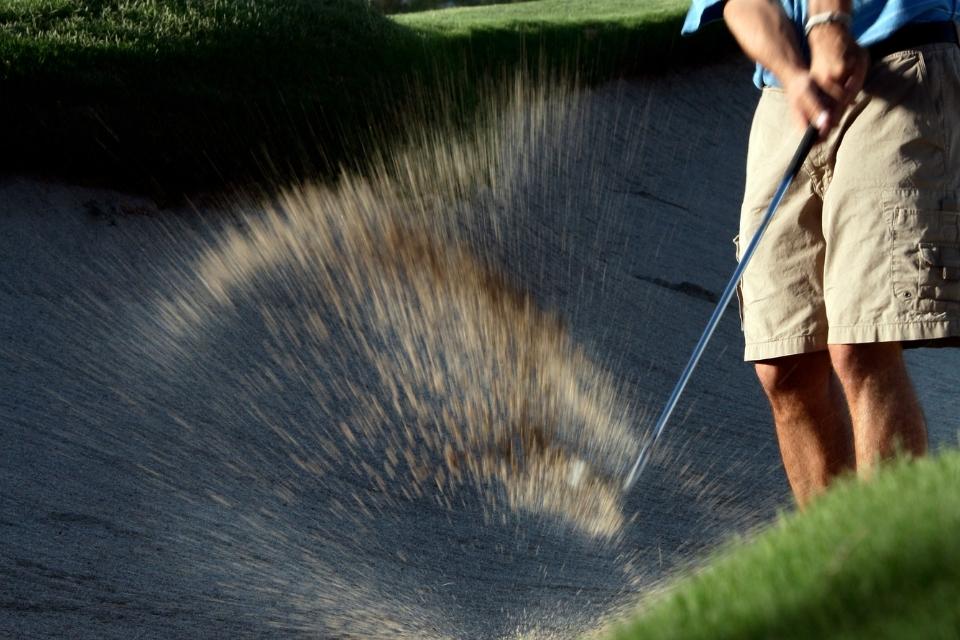 man wearing the best golf shorts hitting out of the bunker